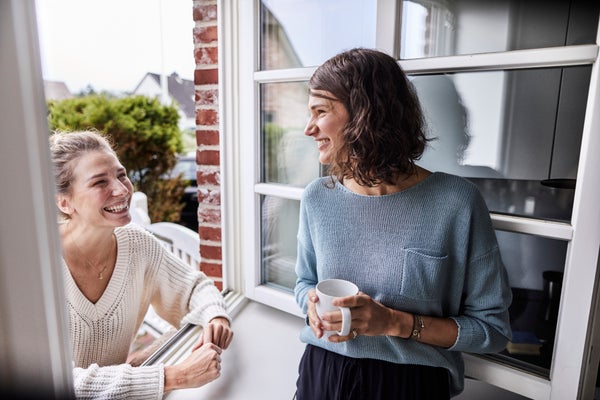 Two women smiling and talking by a window, one holding a mug